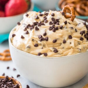 bowl of cookie dough dip topped with mini chocolate chips and a pretzel