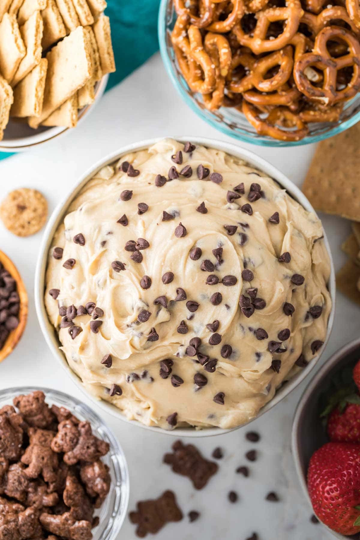 overhead view of cookie dough dip in bowl surrounded by bowls of pretzels, graham crackers, and teddy grahams