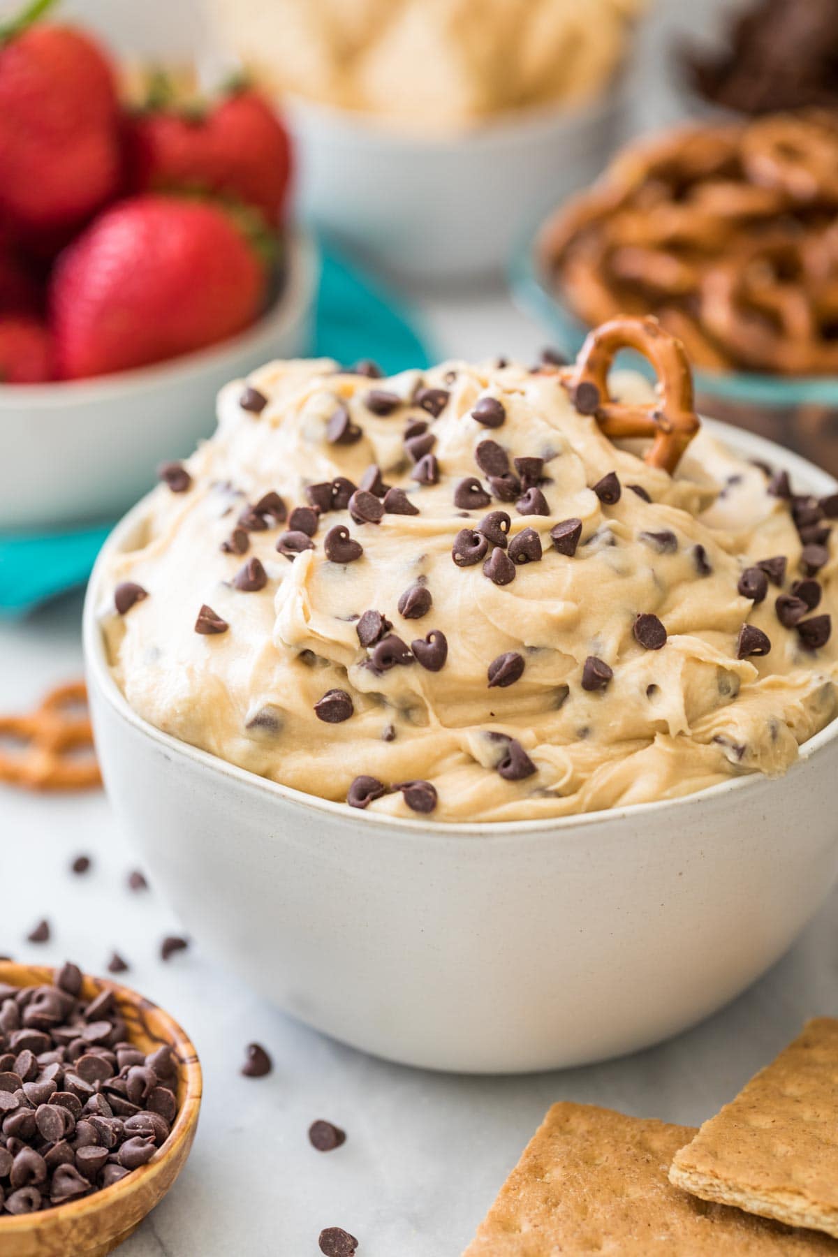 bowl of cookie dough dip topped with mini chocolate chips and a pretzel