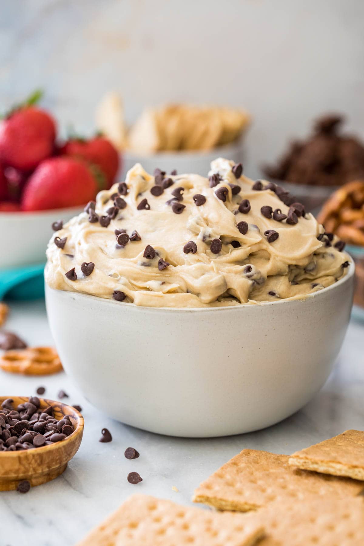 bowl of cookie dough dip with bowls of strawberries, graham crackers, and teddy grahams in the background