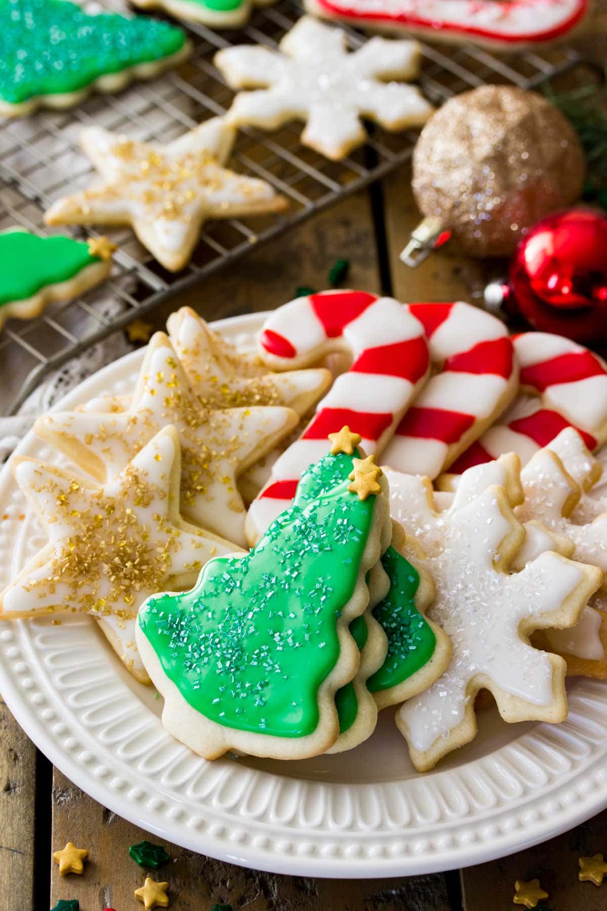 plate of festively iced and decorated sugar cookies next to cooling rack of similar cookies