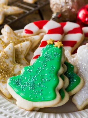 plate of iced and decorated sugar cookies neatly arranged according to type, including christmas trees, gold stars, candy canes, and snowflakes