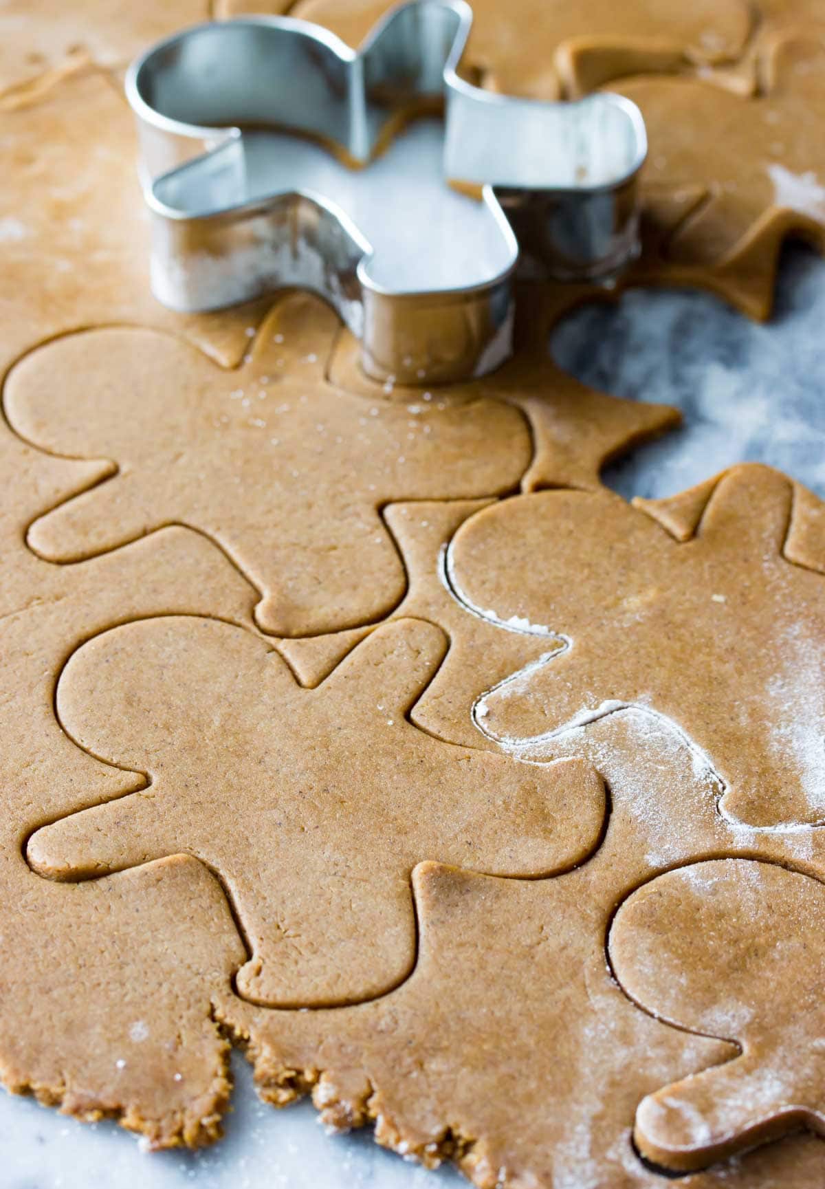 gingerbread men being cut out of dough with cookie cutter