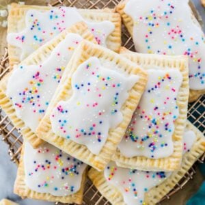 layered pile of homemade strawberry pop tarts topped with rainbow sprinkles on metal cooling rack