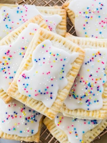 layered pile of homemade strawberry pop tarts topped with rainbow sprinkles on metal cooling rack