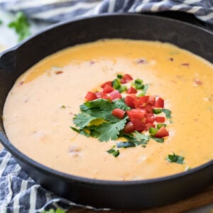 cast iron skillet of homemade queso topped with cilantro and diced tomatoes