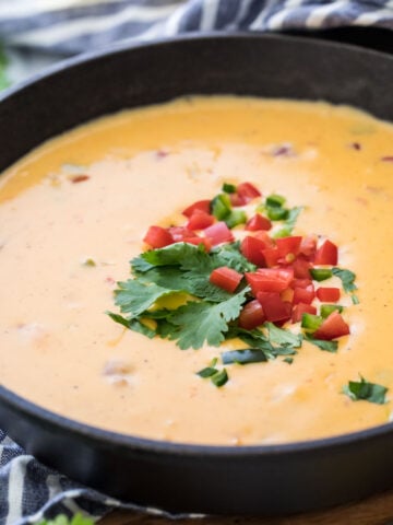 cast iron skillet of homemade queso topped with cilantro and diced tomatoes