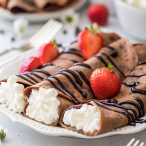 three chocolate crepes rolled and filled with whipped creme topped with chocolate sauce and strawberries