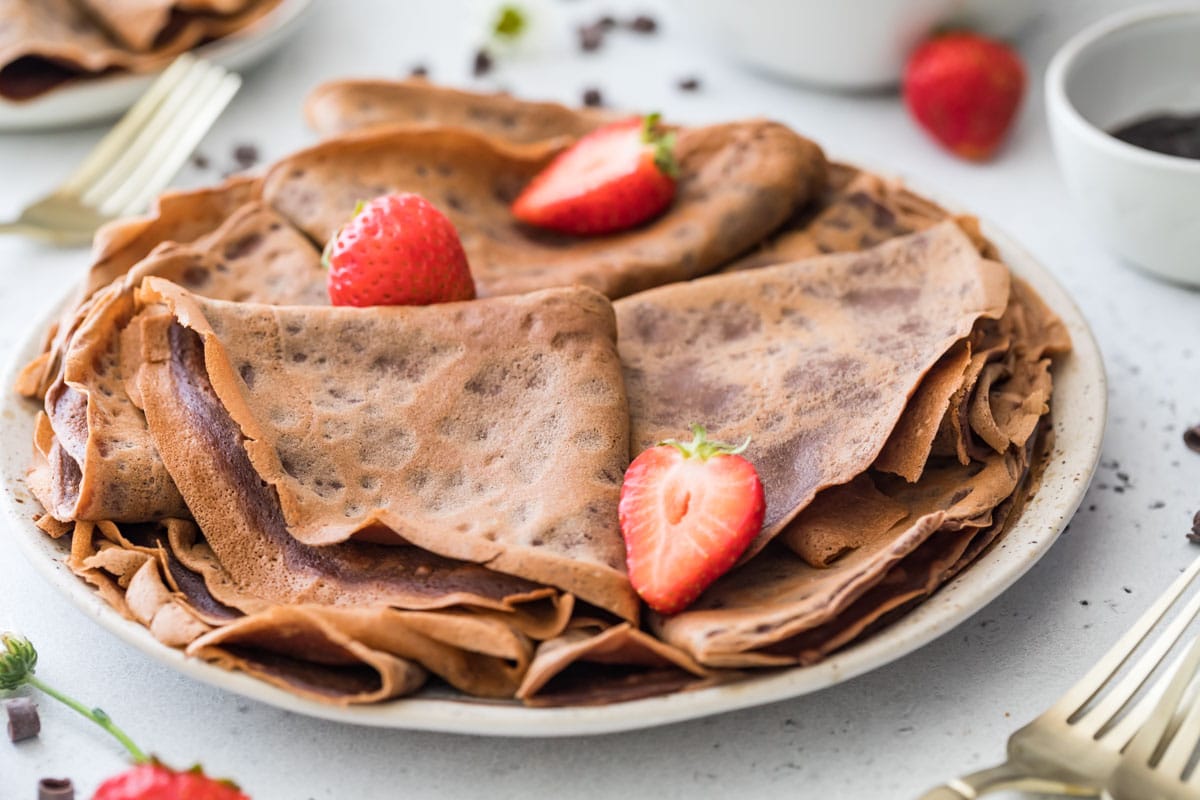 close-up view of a plate stacked with folded chocolate crepes garnished with a few strawberries