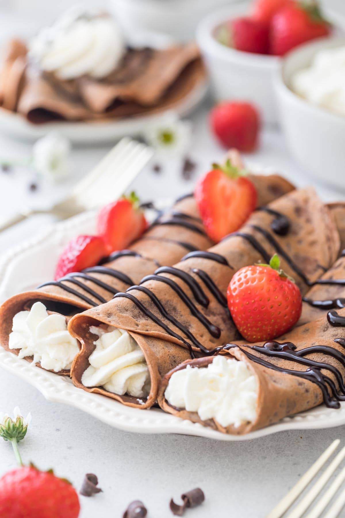 three chocolate crepes rolled and filled with whipped creme topped with chocolate sauce and strawberries