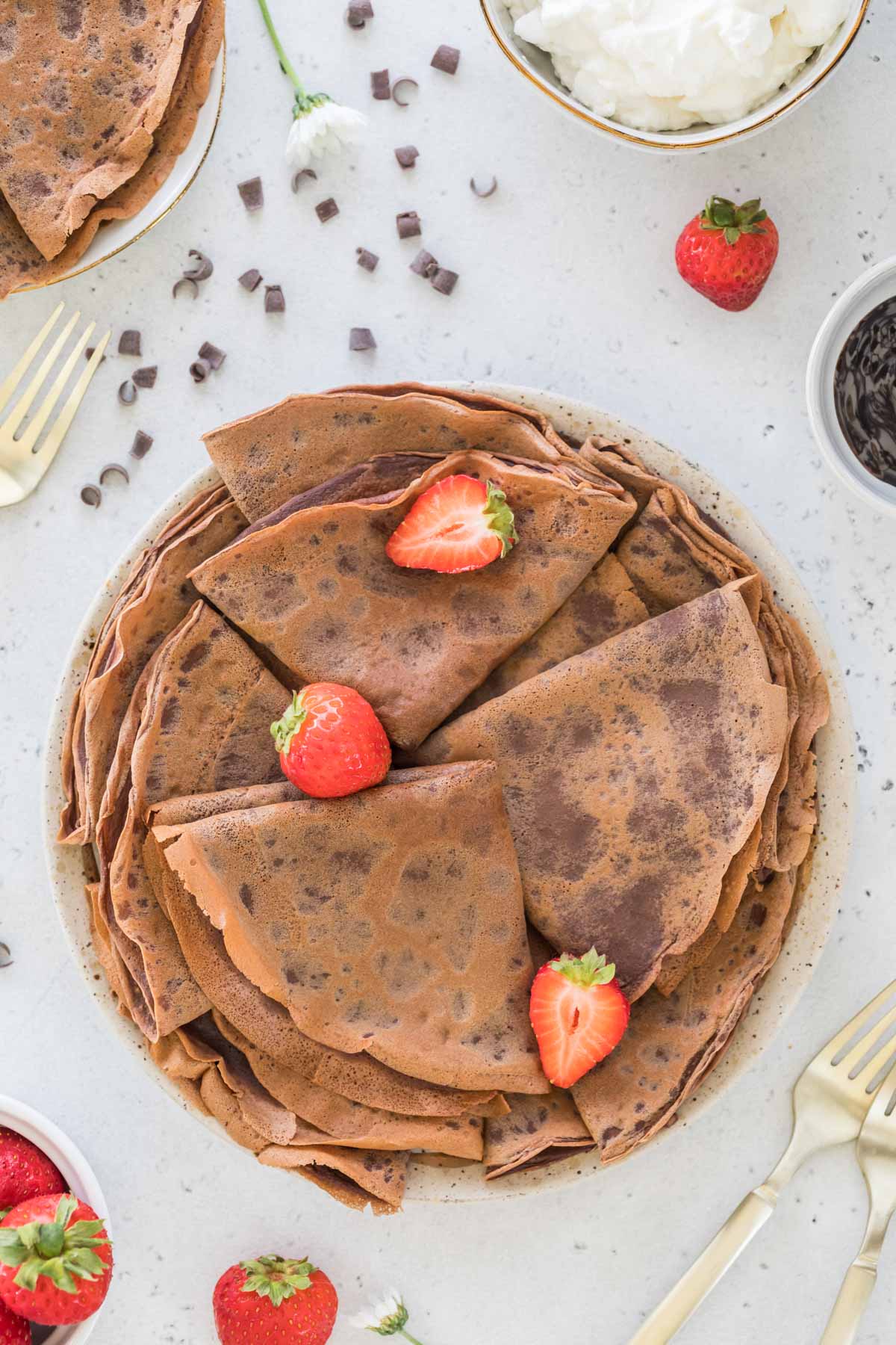 overhead view of a plate full of folded and stacked chocolate crepes topped with a few strawberries