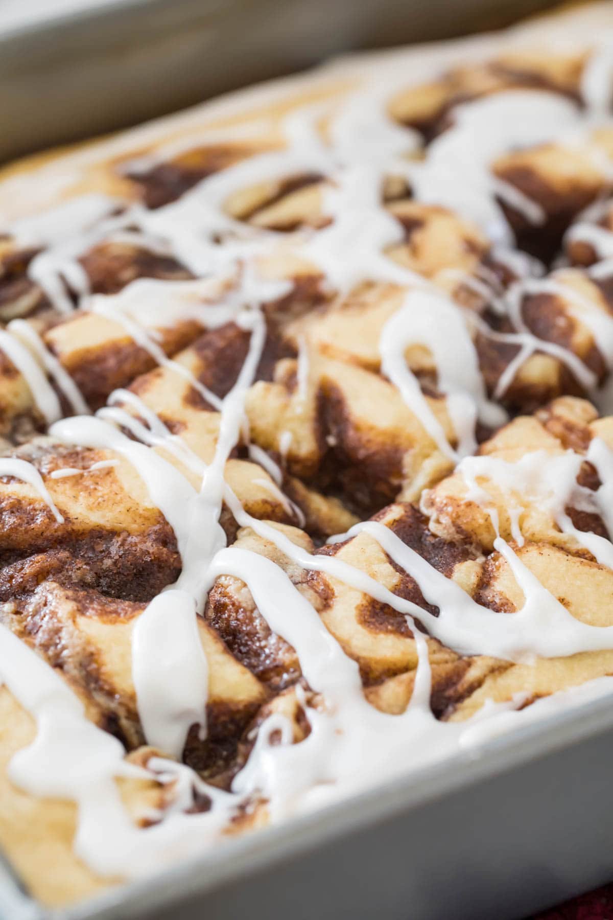 cinnamon roll cake drizzled with white icing before being sliced