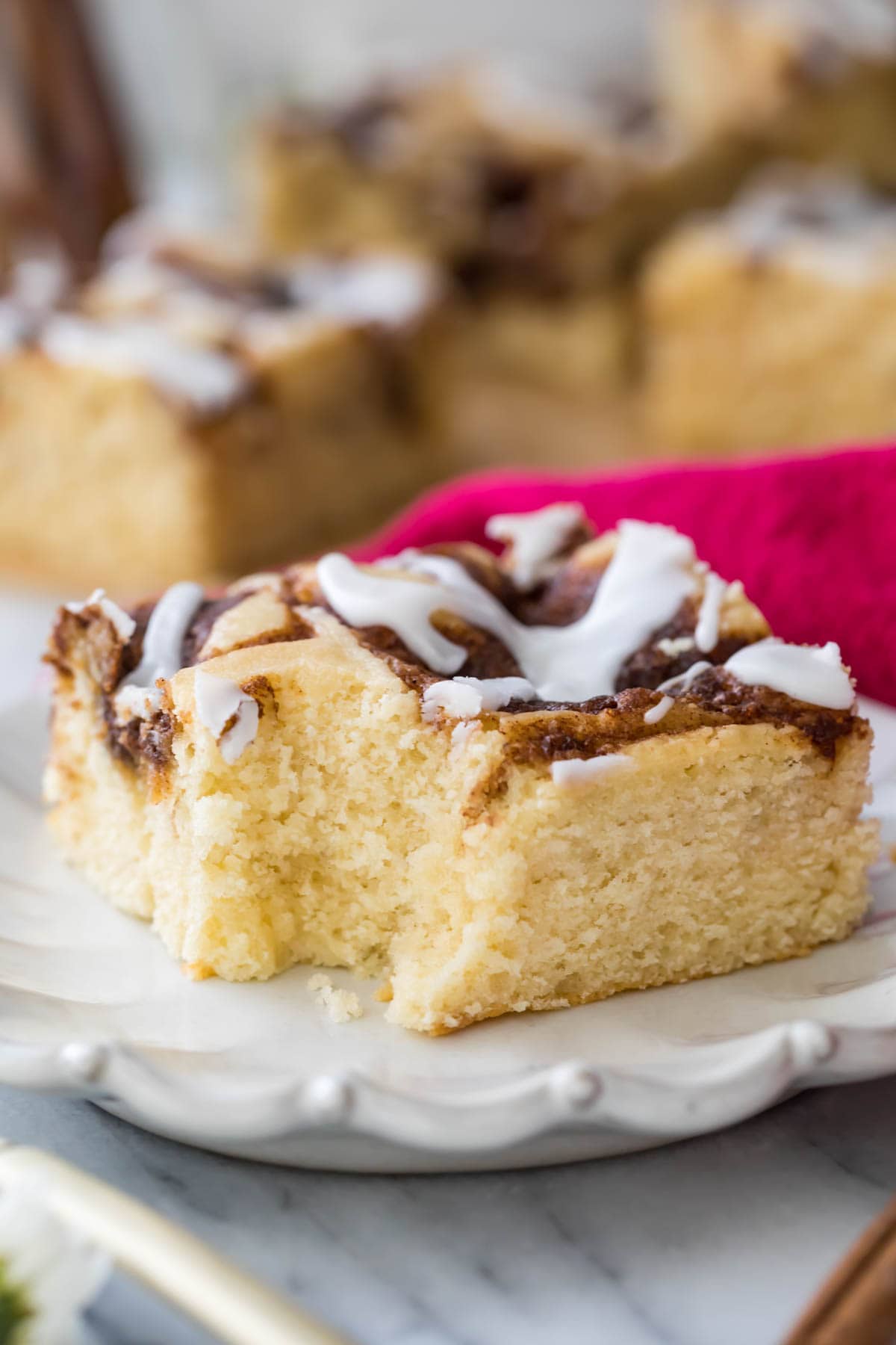 square slice of iced cinnamon roll cake that's missing one bite