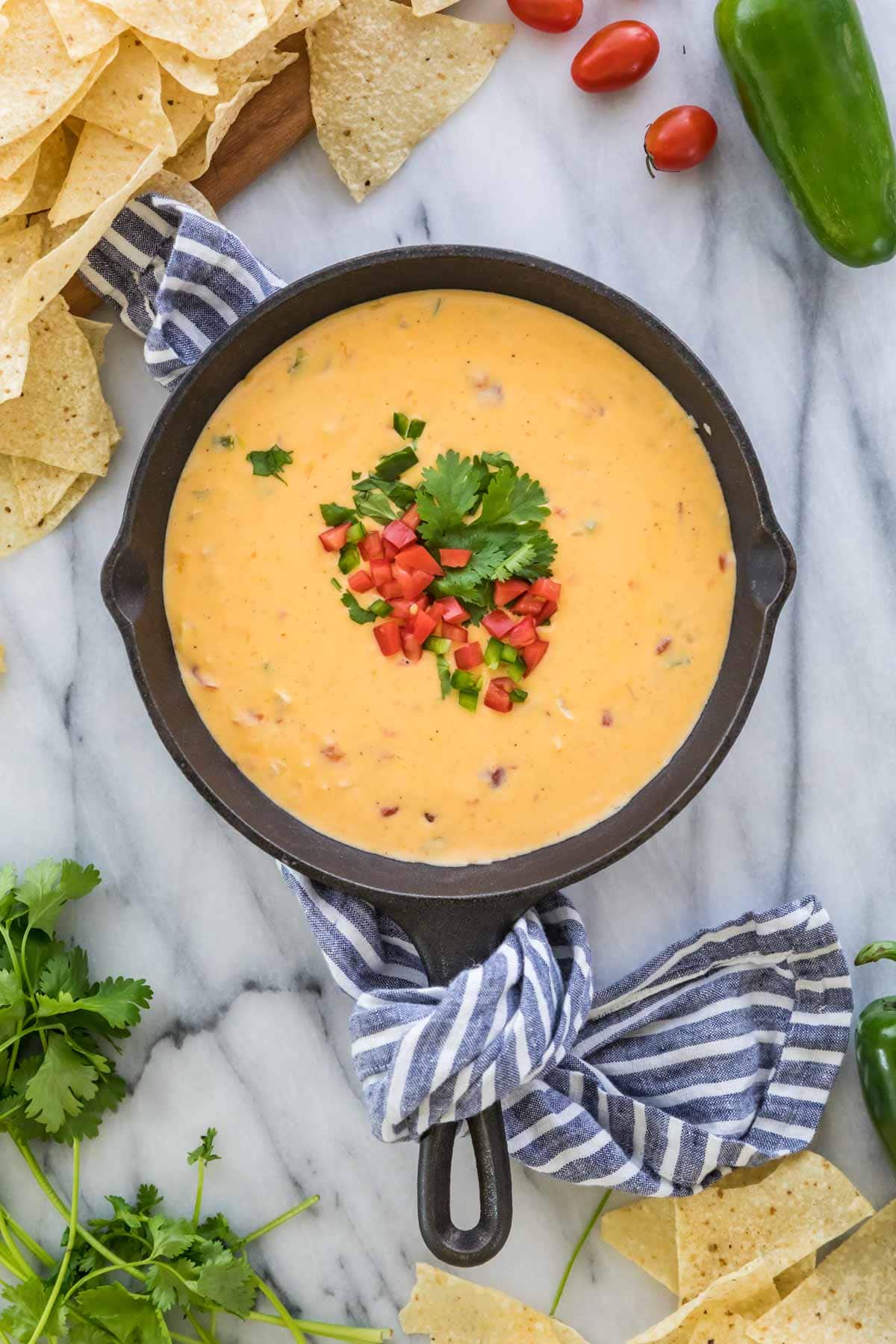 overhead view of a warm skillet full of homemade queso that's been topped with diced tomatoes and cilantro