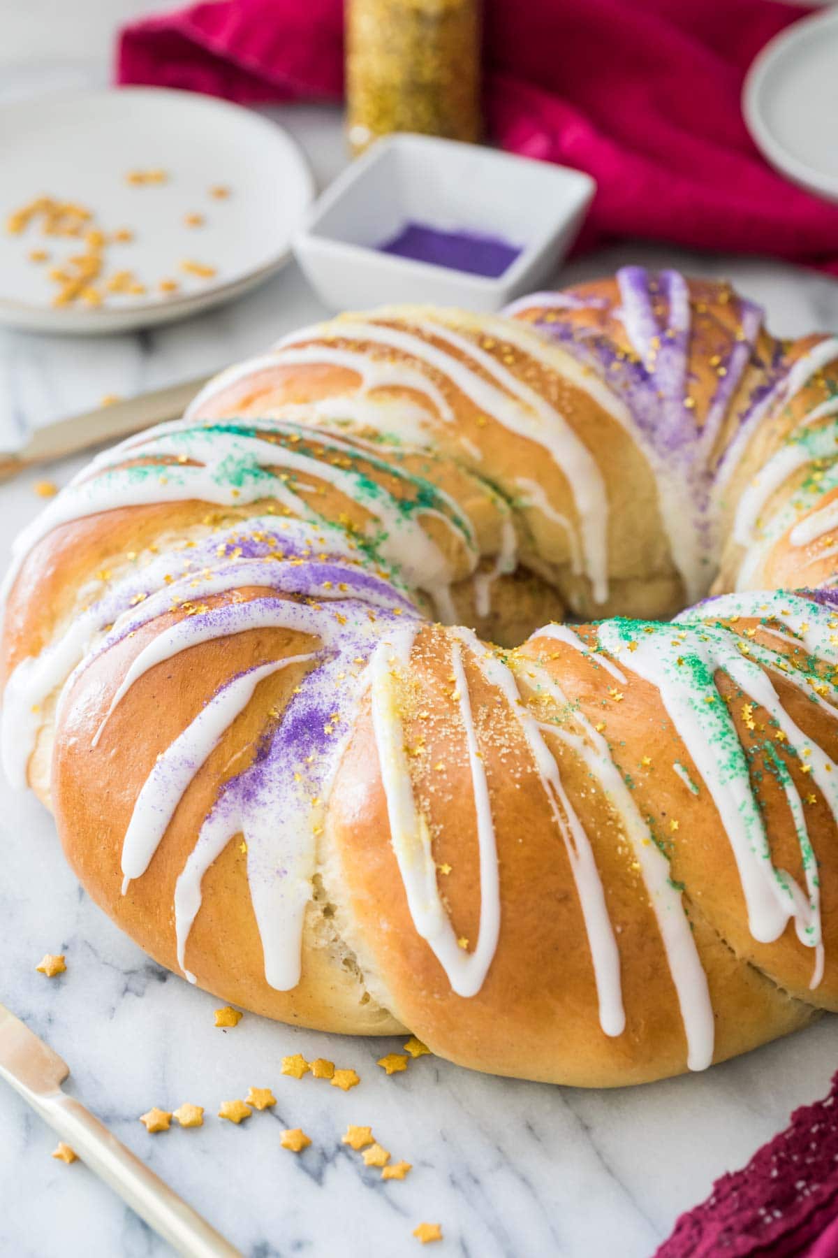 close-up view of golden brown king cake drizzled with white icing and sprinkled with green, purple, and yellow sugars