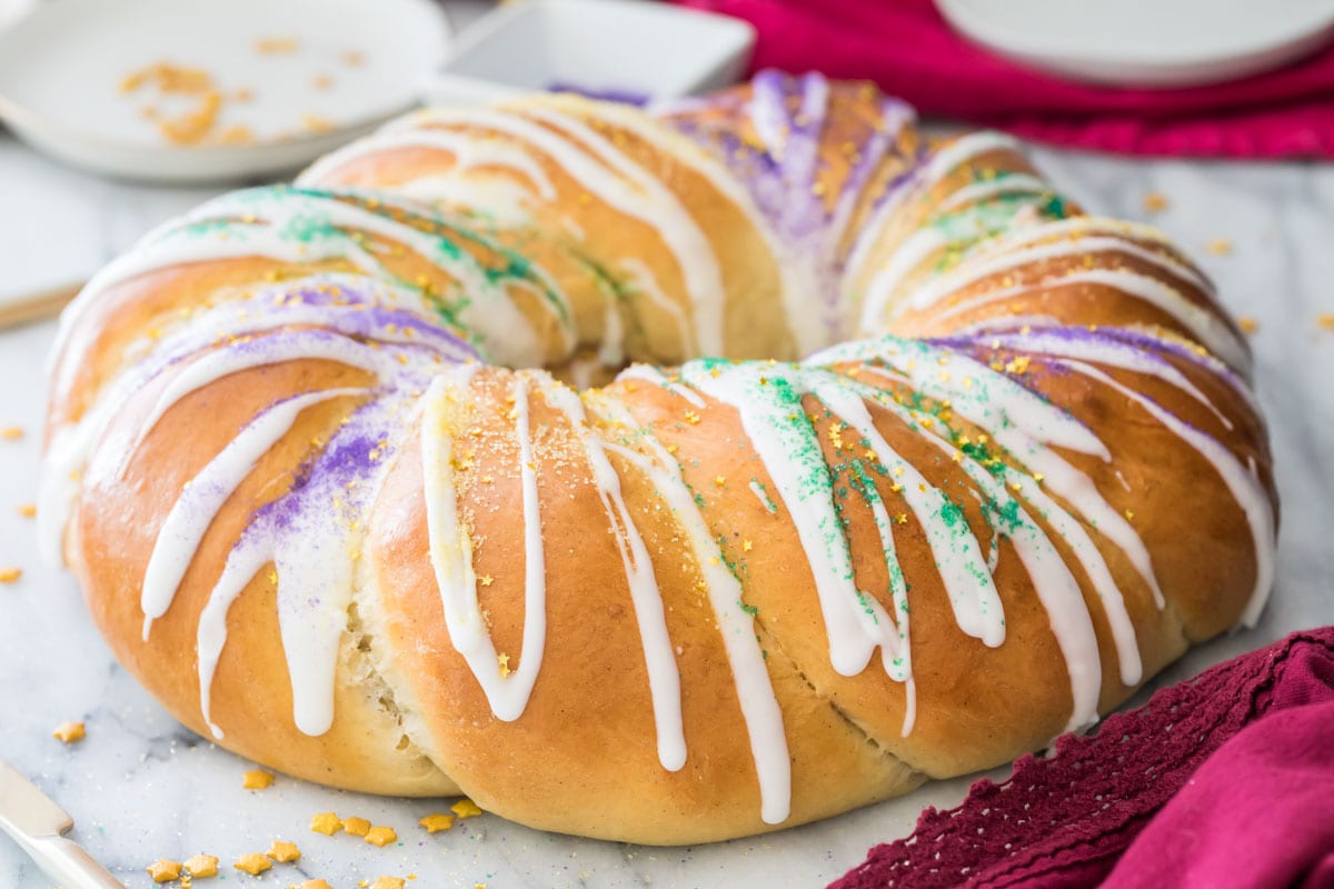 golden brown king cake frosted with white icing and sprinkled with colorful sanding sugars