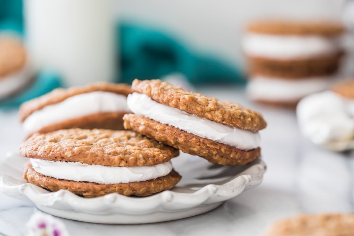 white decorative plate containing three oatmeal cream pies propped against each other with stacked cream pies in the background