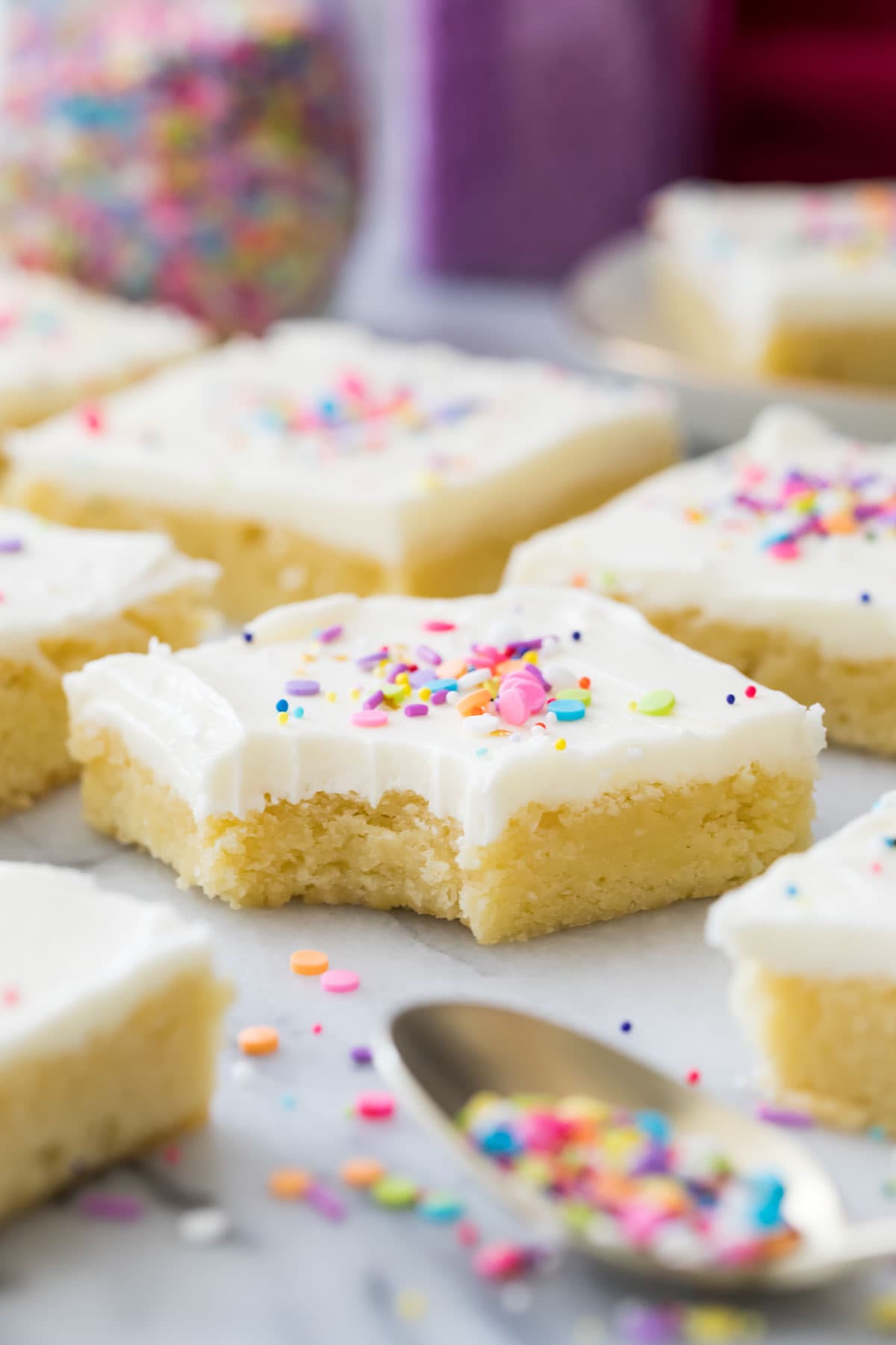 one bite missing from a frosted sugar cookie bar topped with rainbow sprinkles