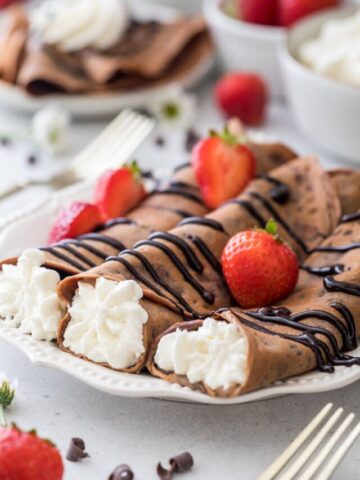 three chocolate crepes rolled and filled with whipped creme topped with chocolate sauce and strawberries