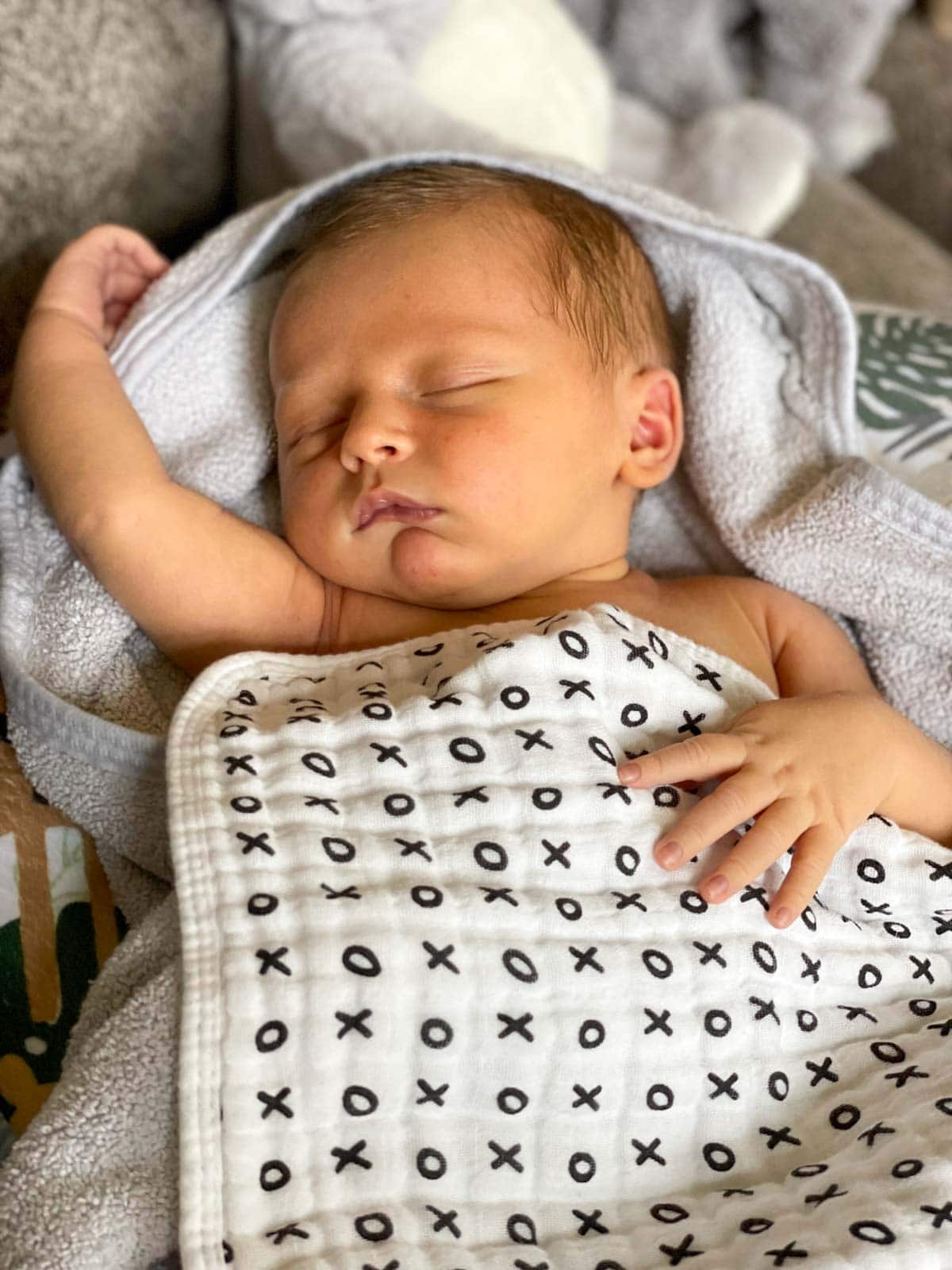 newborn baby with arm raised above head sleeping on white towel