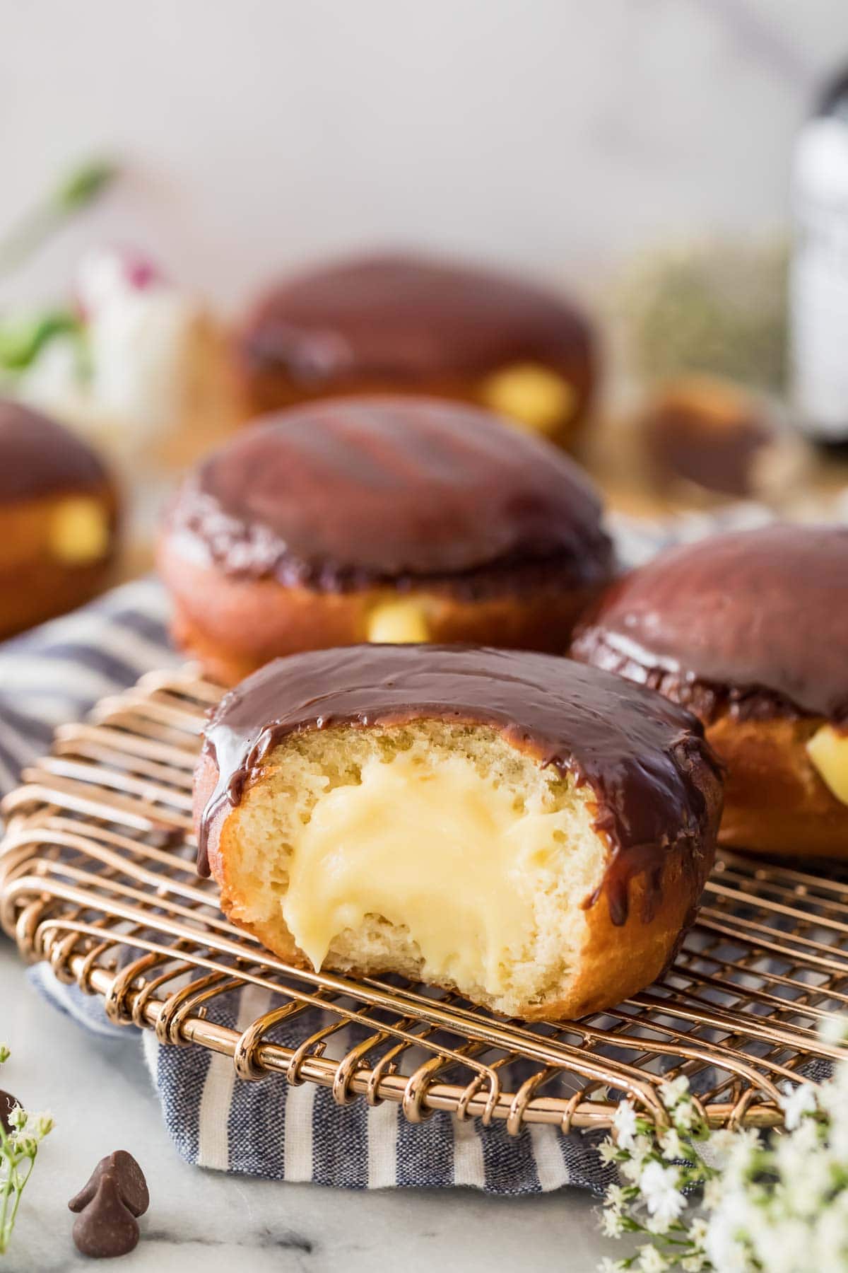 Boston cream donuts on a metal cooling rack, with one missing a large bite to show the pastry cream filling