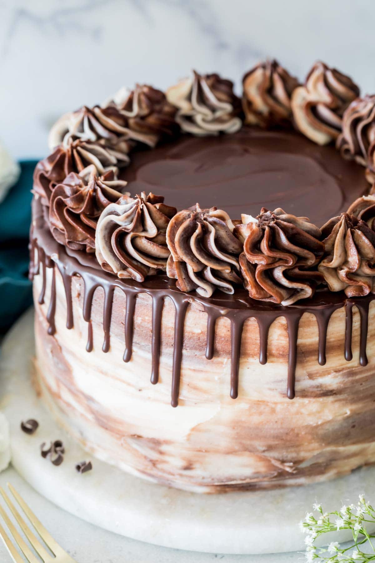 swirled chocolate cream cheese icing covering a cheesecake stuffed cake topped with a chocolate ganache drop and swirled icing dollops