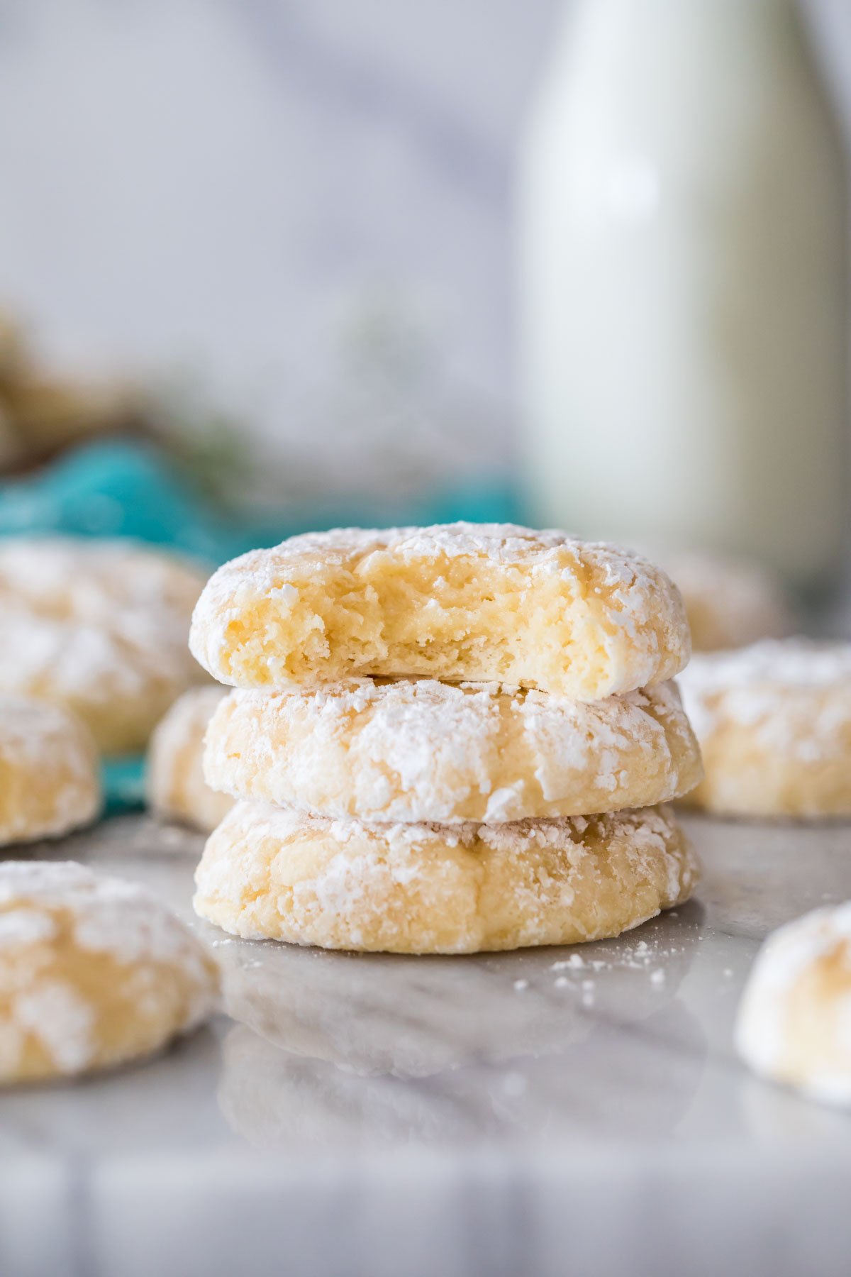 three vertically stacked gooey butter cookies on a white marble surface surrounded by other cookies and a milk jug in the background