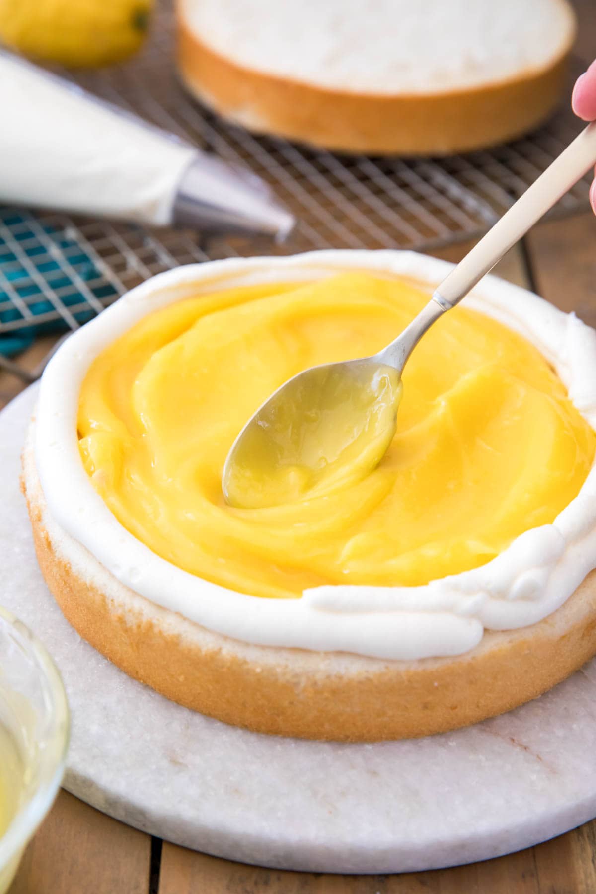 spoon spreading lemon curd onto a layer cake piped with a white icing dam