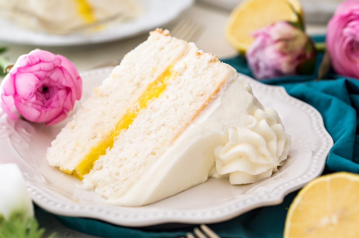 slice of white cake filled with lemon curd and iced with a whipped cream cheese frosting surrounded by pink flowers