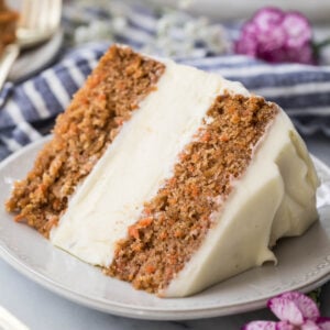 slice of carrot cake cheesecake frosted with cream cheese icing on a white plate