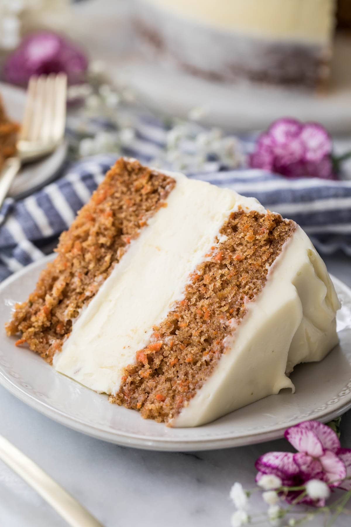 slice of carrot cake cheesecake frosted with cream cheese icing on a white plate