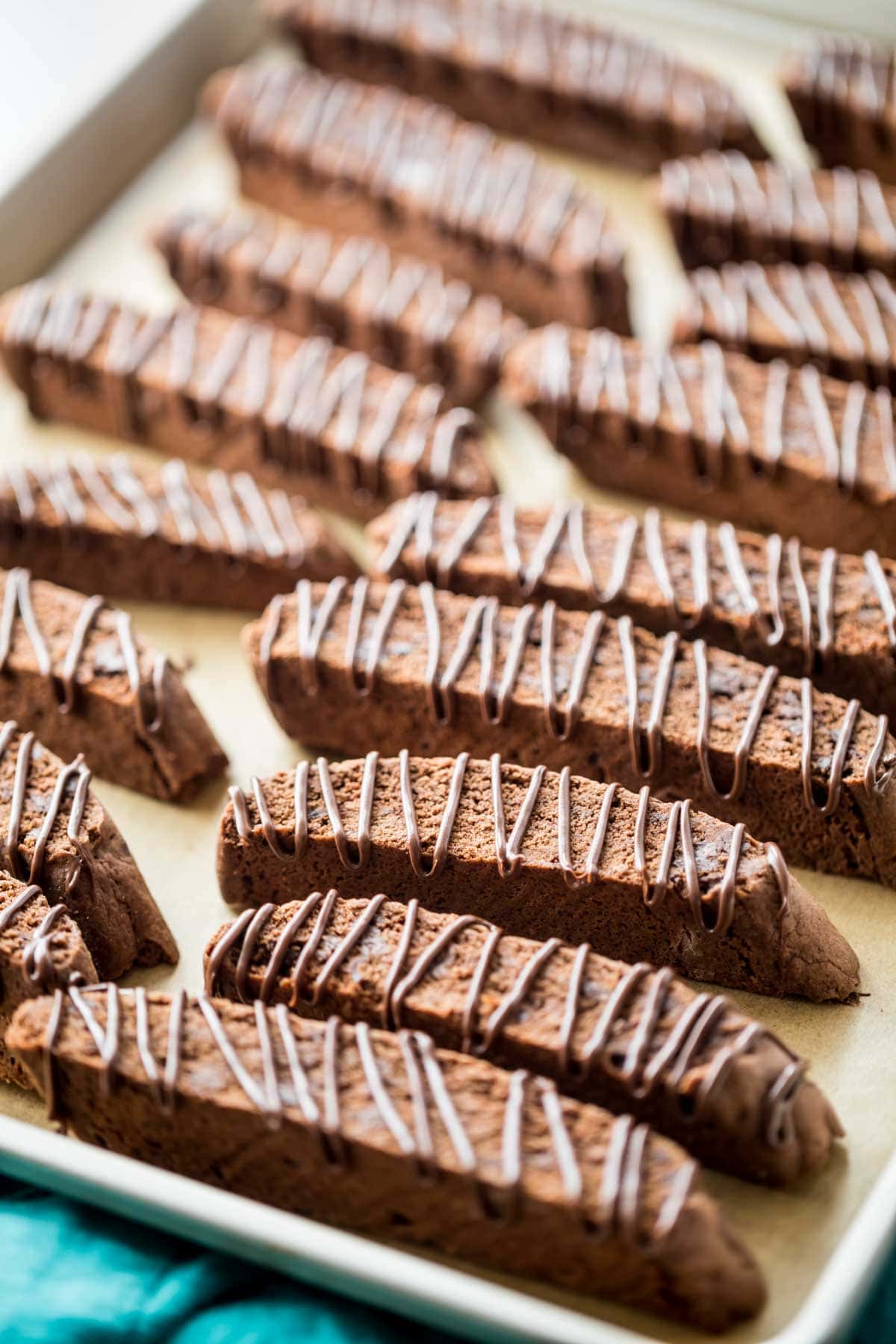 chocolate drizzled chocolate biscotti cookies arranged on a baking sheet