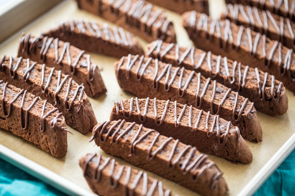 chocolate drizzled chocolate biscotti cookies arranged on a baking sheet