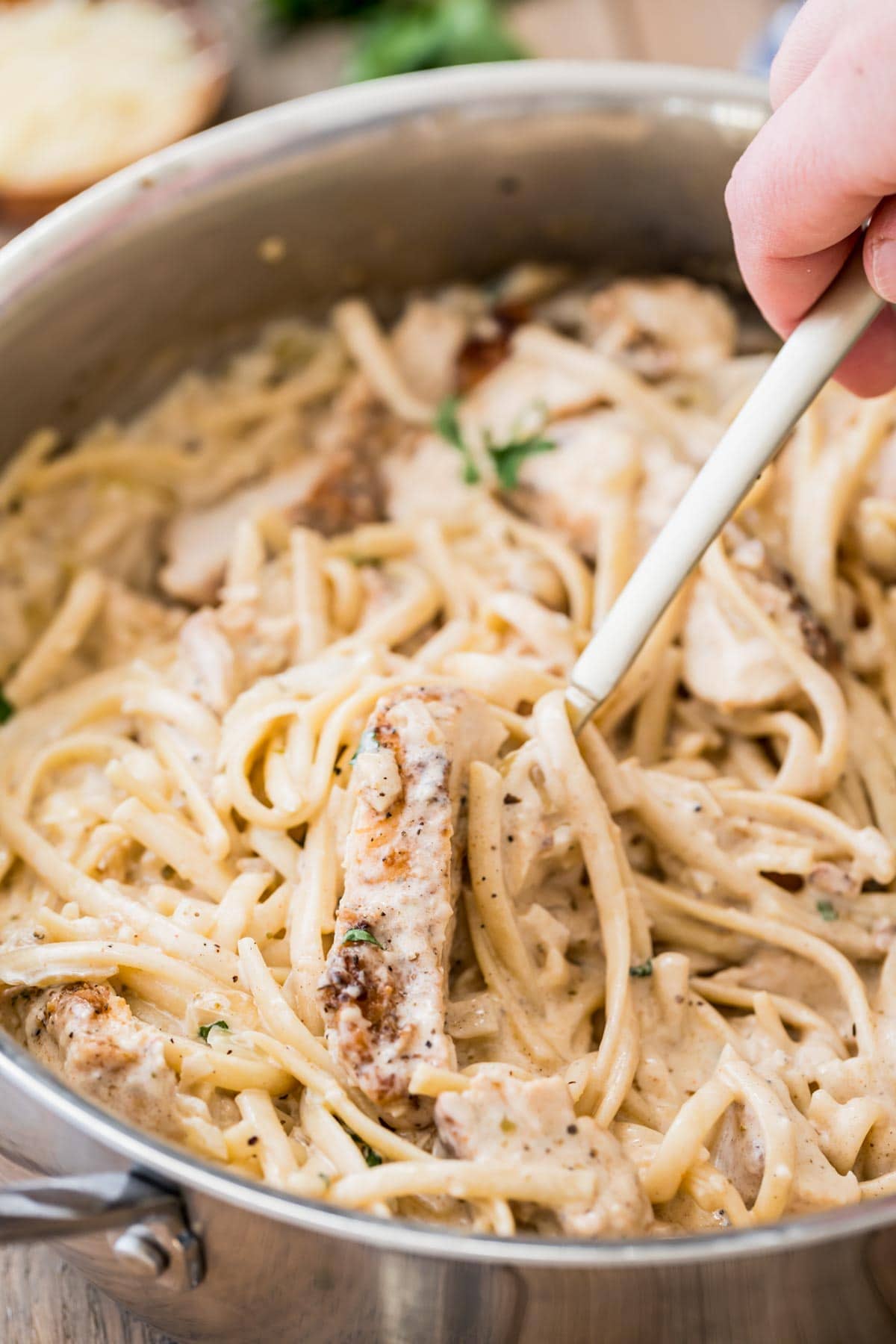 fork scooping a serving of creamy chicken pasta from a stainless steel skillet