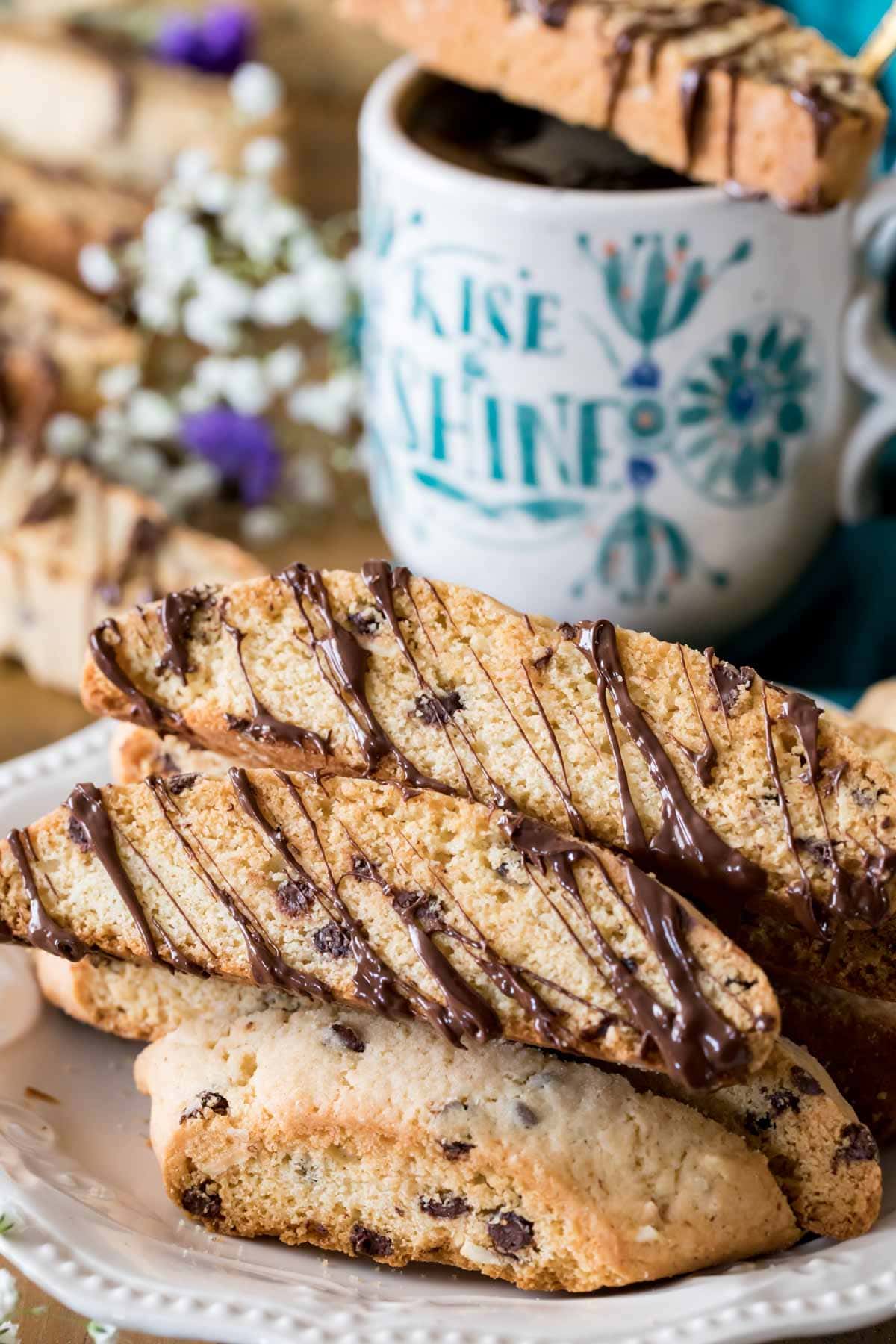 stack of chocolate chip biscotti cookies drizzled with chocolate beside a cofree mug
