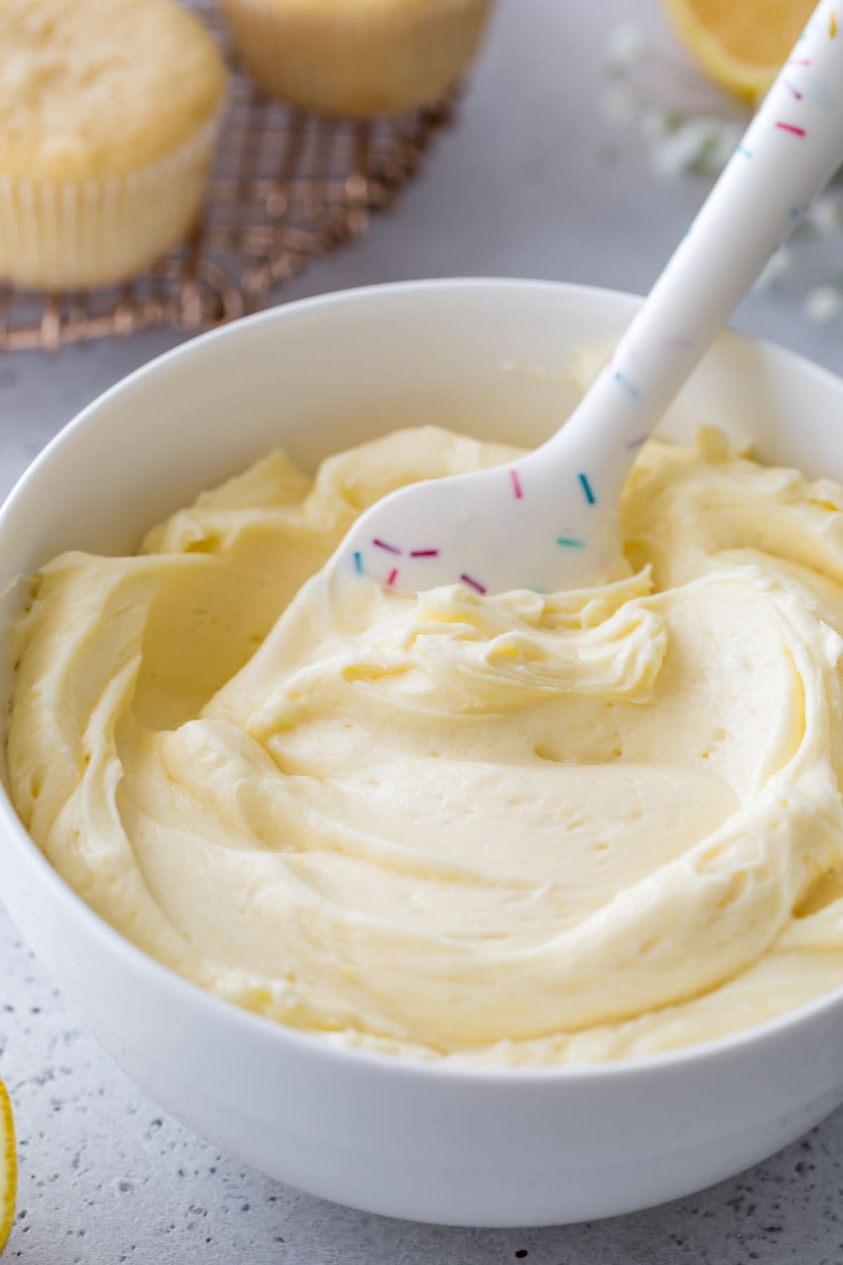 white bowl full of pale yellow frosting being stirred by a spatula