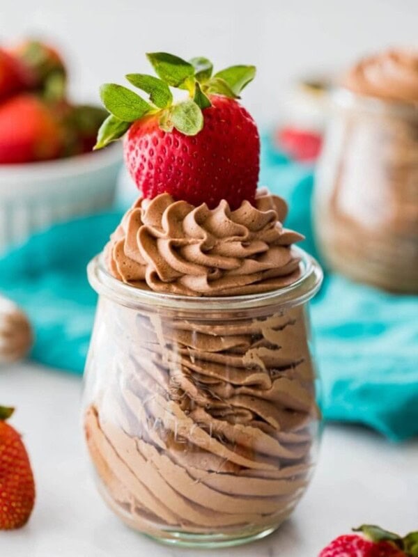 small glass jar filled with chocolate flavored whipped cream and garnished with a ripe strawberry