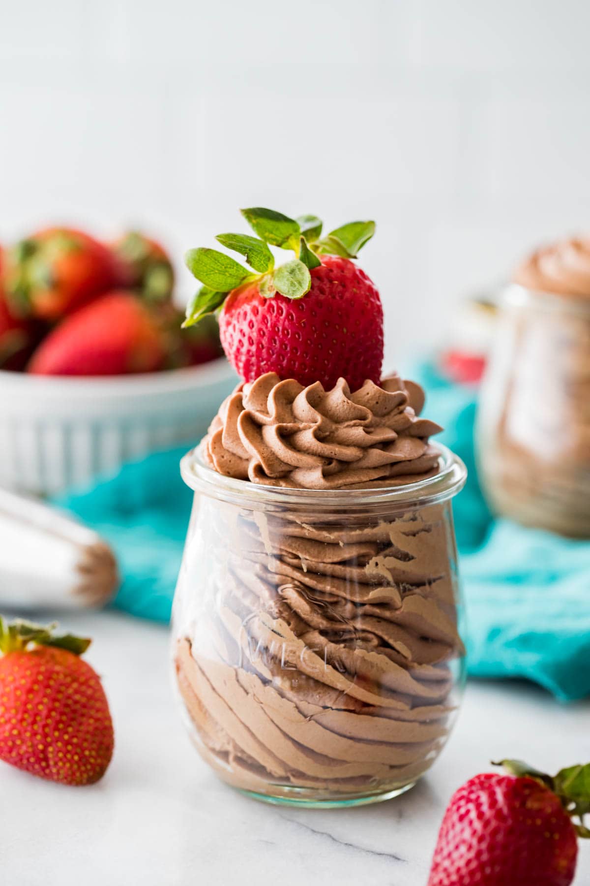 small glass jar filled with chocolate flavored whipped cream and garnished with a ripe strawberry