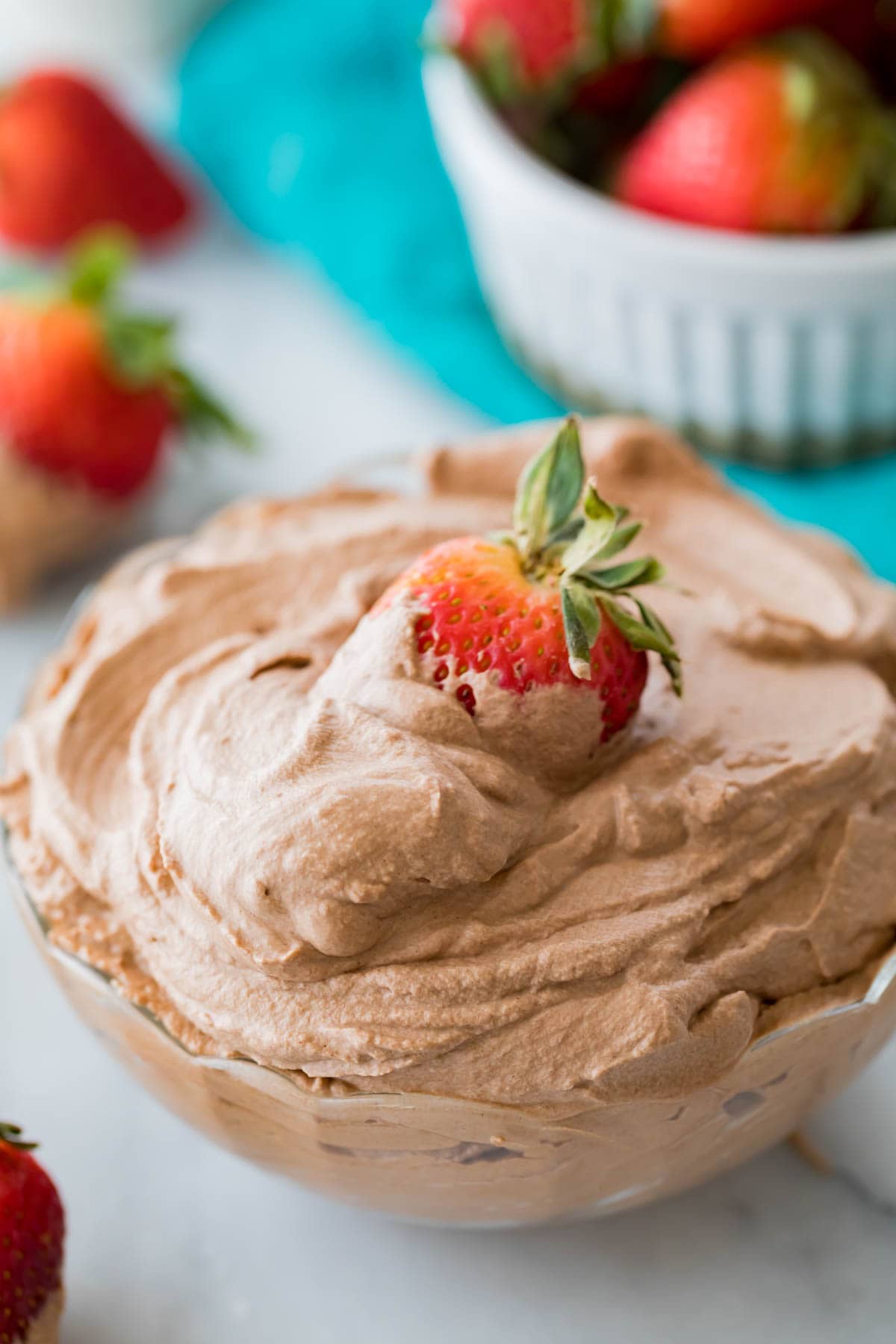 a ripe strawberry being dipped into a thick bowl of chocolate flavored whipped cream