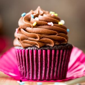 head-on view of a chocolate cupcake in a hot pink cupcake wrapper topped with piped chocolate frosting and rainbow sprinkles