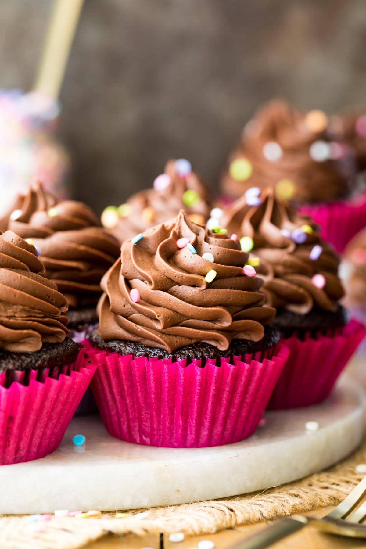 three chocolatey cupcakes topped with chocolate frosting and sprinkles on a white platter