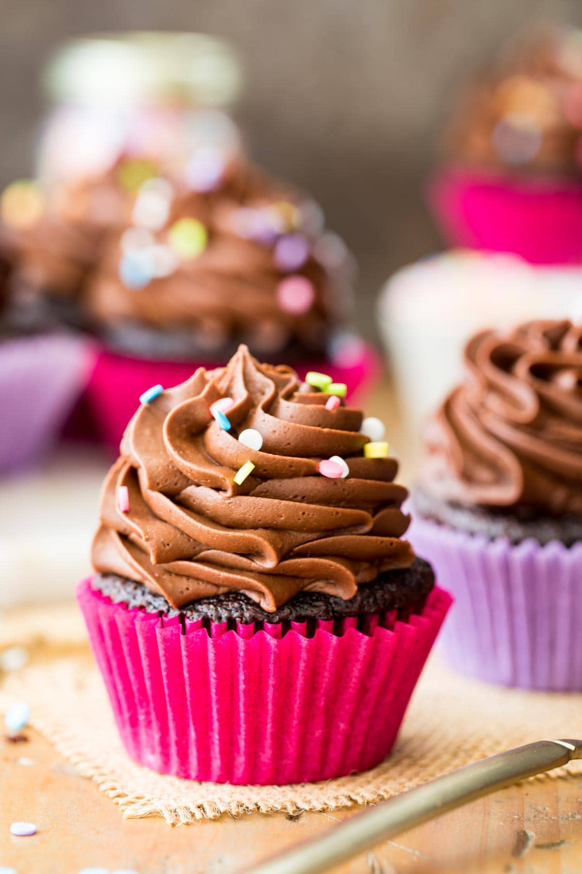 cupcakes in pink and purple cupcake wrappers topped with piped frosting and sprinkles