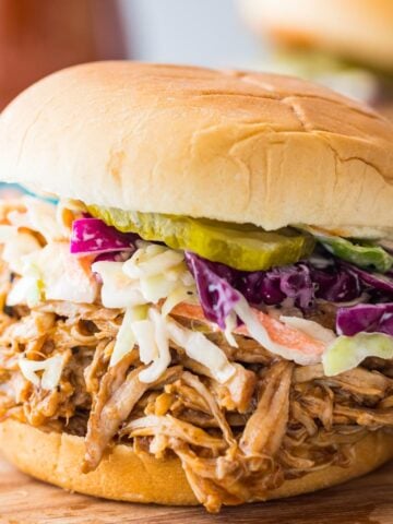 instant pot pulled pork on a sandwich topped with homemade coleslaw and pickles