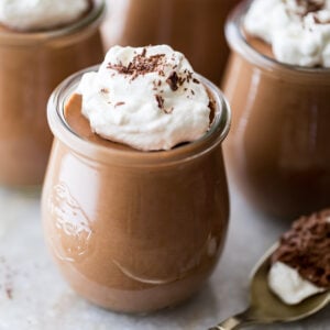 small glass jars of chocolate mousse topped with whipped cream and chocolate shavings