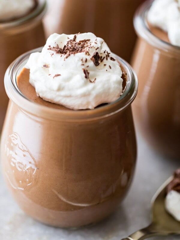 small glass jars of chocolate mousse topped with whipped cream and chocolate shavings