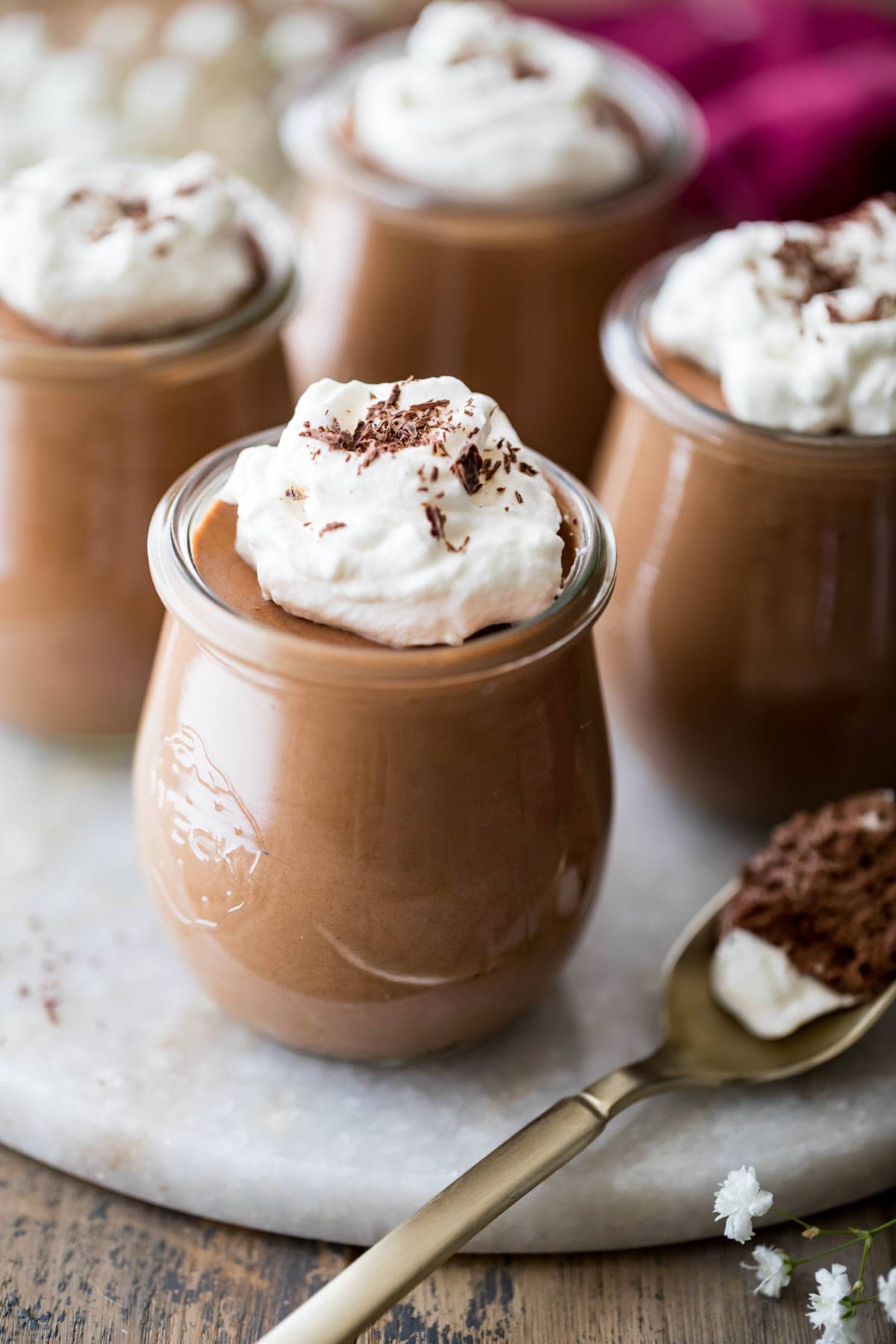 small glass jars of chocolate mousse topped with whipped cream and chocolate shavings