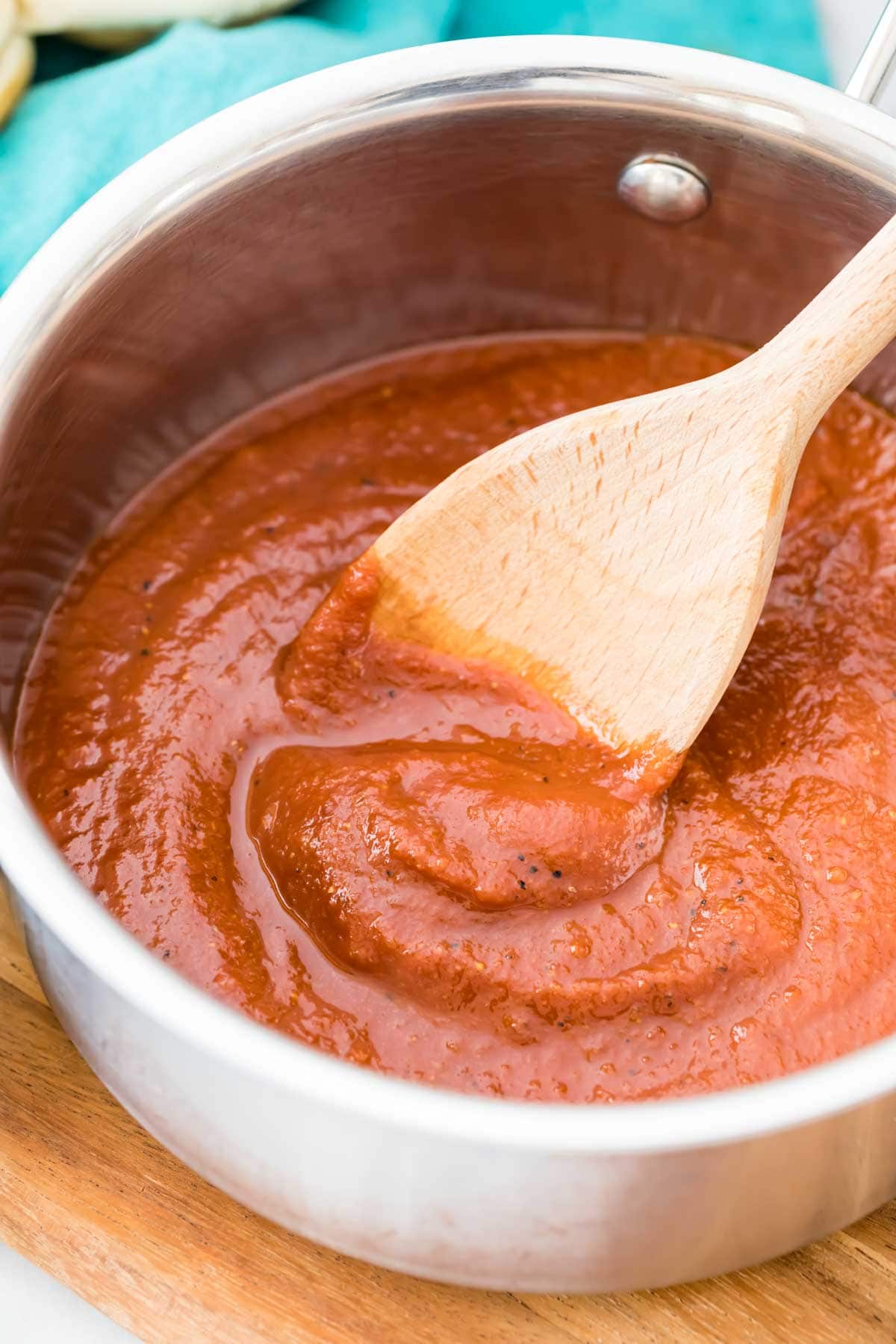 metal pot of barbecue sauce being stirred by a wooden spoon