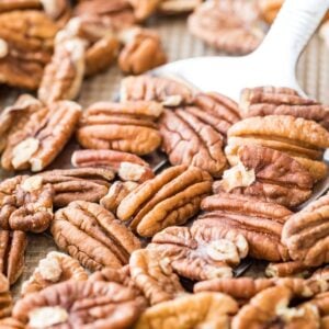 photo showing how to toast pecans in the oven, with a metal spatula about to flip whole pecans on a baking sheet