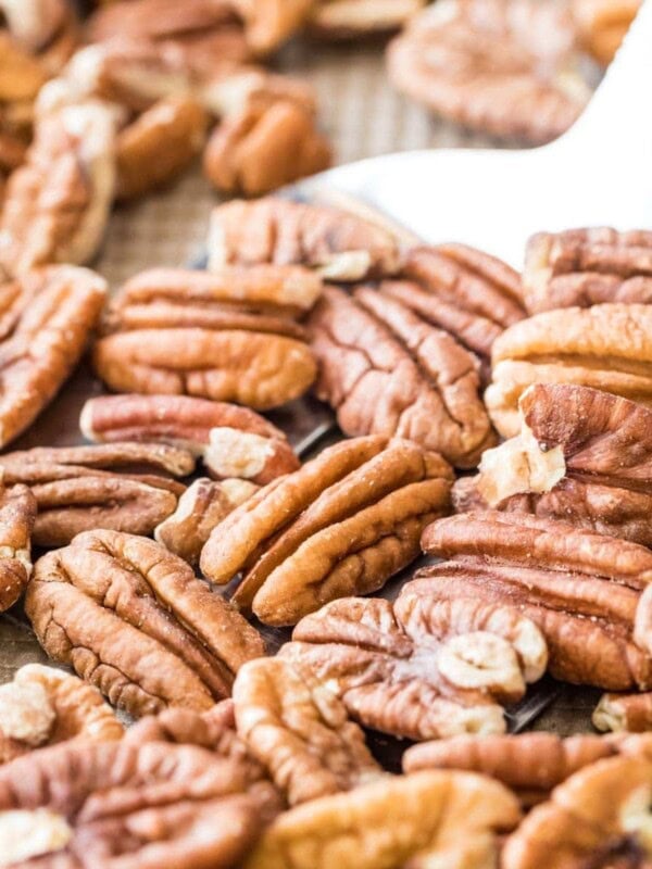photo showing how to toast pecans in the oven, with a metal spatula about to flip whole pecans on a baking sheet