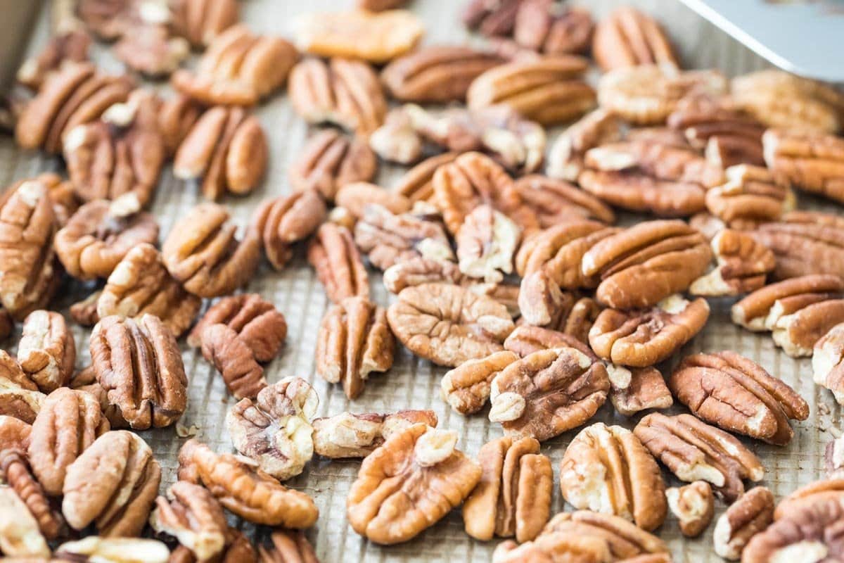 whole pecans scattered across a baking sheet